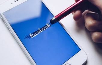 Hand using a stylus to cross out the word "facebook"
