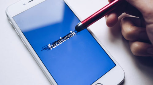 Hand using a stylus to cross out the word "facebook"