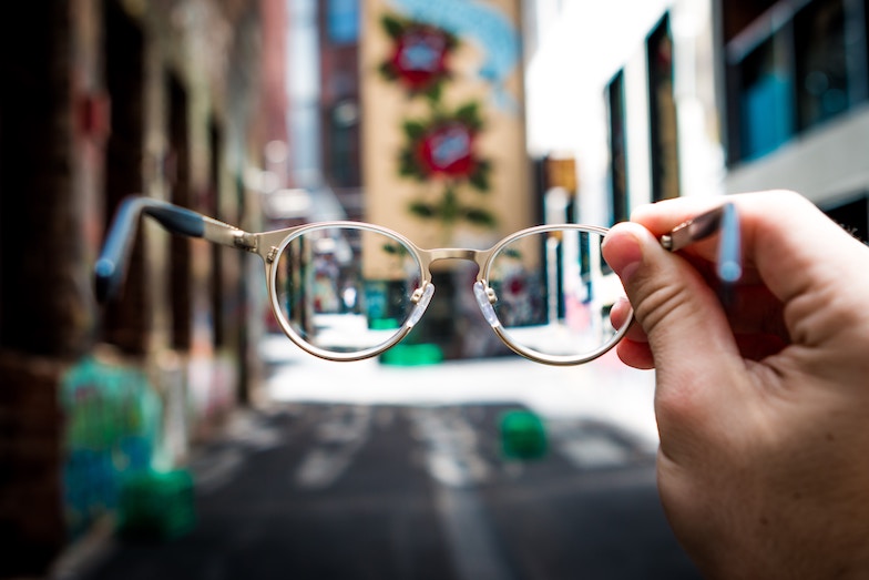 A hand holding a pair of glasses in the center of a street, vision concept