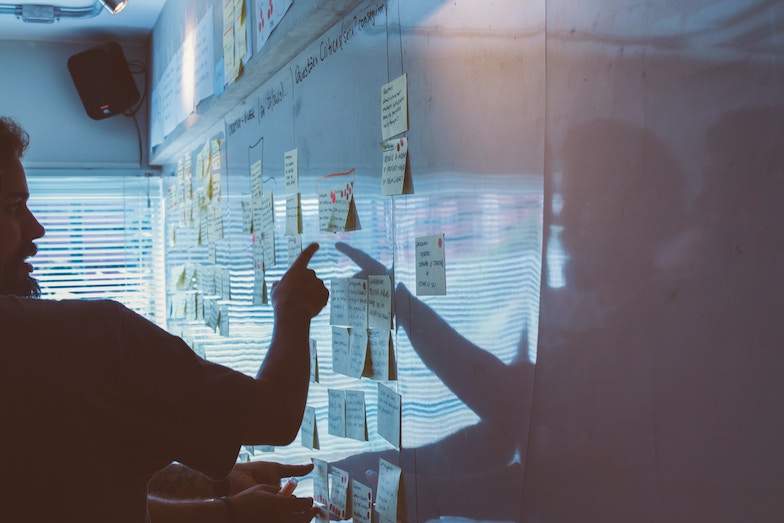 Bearded man pointing at post-it notes on a whiteboard quizzically